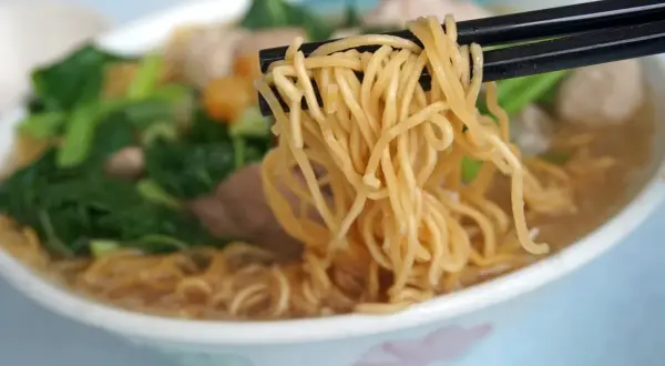 Chopsticks unoszą kłębek złocistego makaronu z miski pełnej aromatycznej domowej zupki chińskiej z warzywami i mięsem.