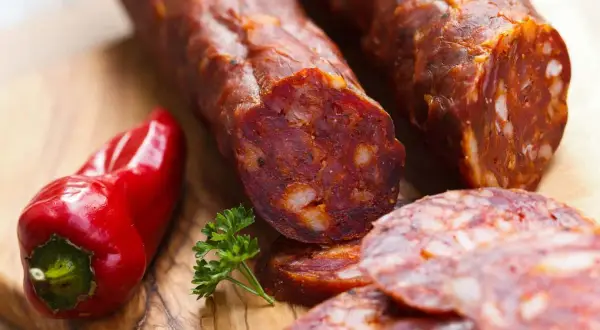 Kawałki pikantnego chorizo, czerwona papryczka i natka pietruszki na desce. To właśnie chorizo, co to za przysmak!