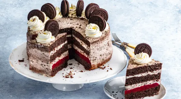 Pyszny tort oreo z kremem, malinową warstwą i ciasteczkami oreo na wierzchu. Kawałek ciasta na talerzyku.