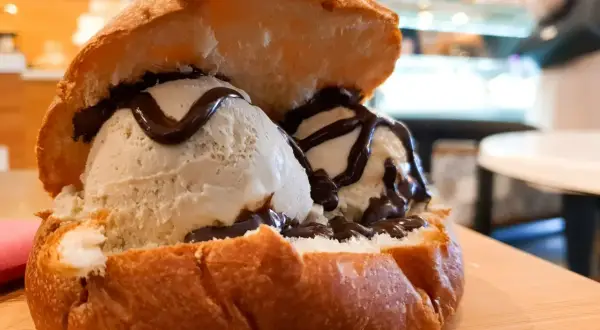 Pyszne lody w brioszce, polane czekoladą, na drewnianej desce.