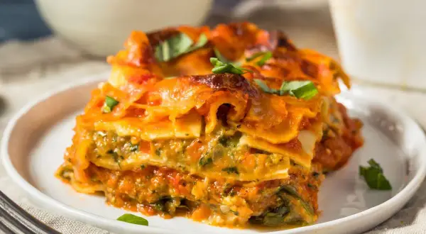 Pyszna lasagne wegetariańska z warzywami i sosem pomidorowym, udekorowana świeżą bazylią.