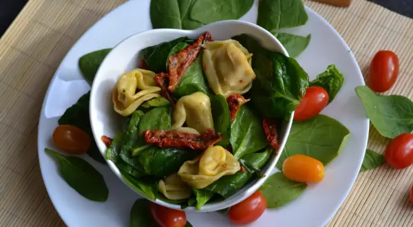 Pyszne tortellini z suszonymi pomidorami i świeżym szpinakiem, ozdobione pomidorkami koktajlowymi.