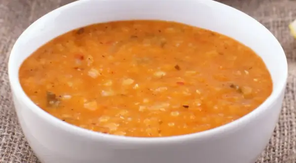 Gęsta, pomarańczowa zupa dhal w białej misce, podana na lnianym obrusie.