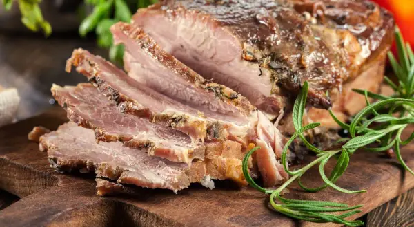 Pokrojony, pieczony boczek z ziołami na desce. Idealny przykład, jak zapeklować boczek do pieczenia, by był soczysty i aromatyczny.