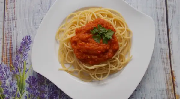 Spaghetti ze świeżych pomidorów, udekorowane natką pietruszki, na białym talerzu, na tle drewnianego blatu i lawendy.
