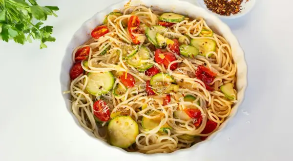 Pyszny makaron z cukinią, pomidorkami i parmezanem, posypany płatkami chili.