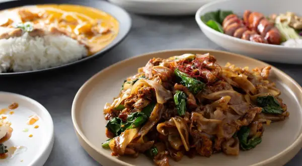 Pyszny pad thai makaron z kurczakiem i warzywami, podany na talerzu. Obok widać inne dania.