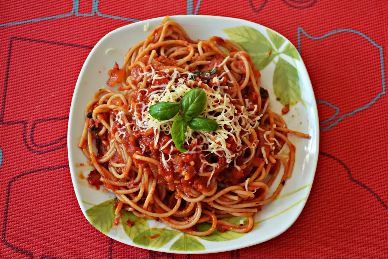 Pyszne spaghetti z pomidorami, posypane startym serem i udekorowane listkami bazylii. Idealne na szybki obiad.
