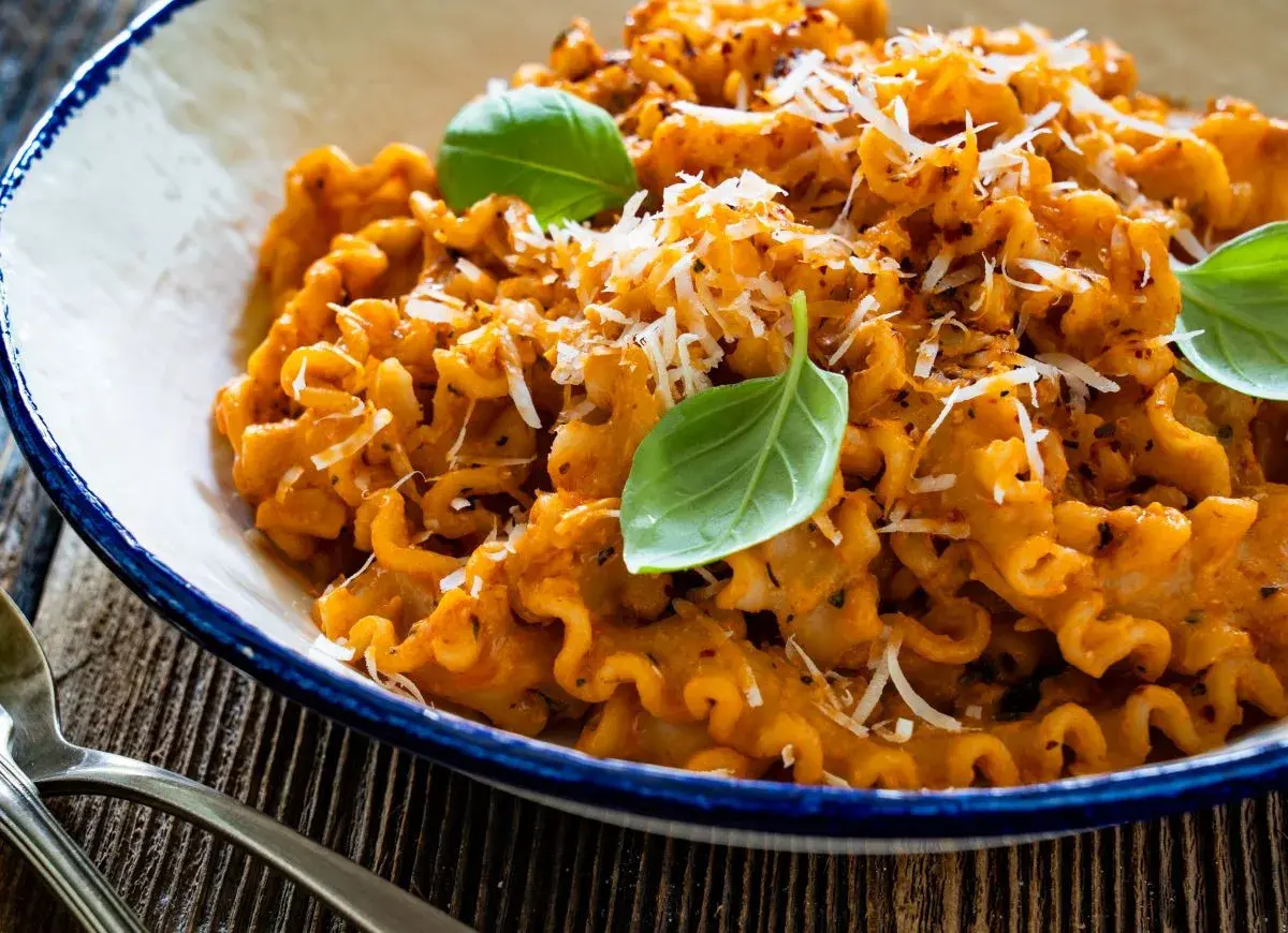 Pyszna włoska pasta z sosem pomidorowym, posypana parmezanem i udekorowana listkami bazylii. Idealna na obiad.