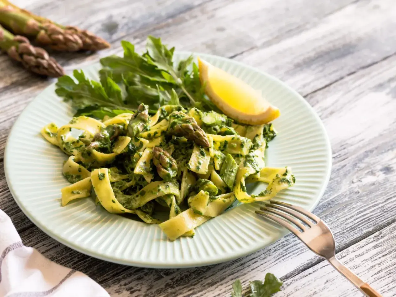 Pyszny makaron ze szparagami i zielonym pesto, udekorowany cytryną i rukolą. Idealne danie na wiosnę.