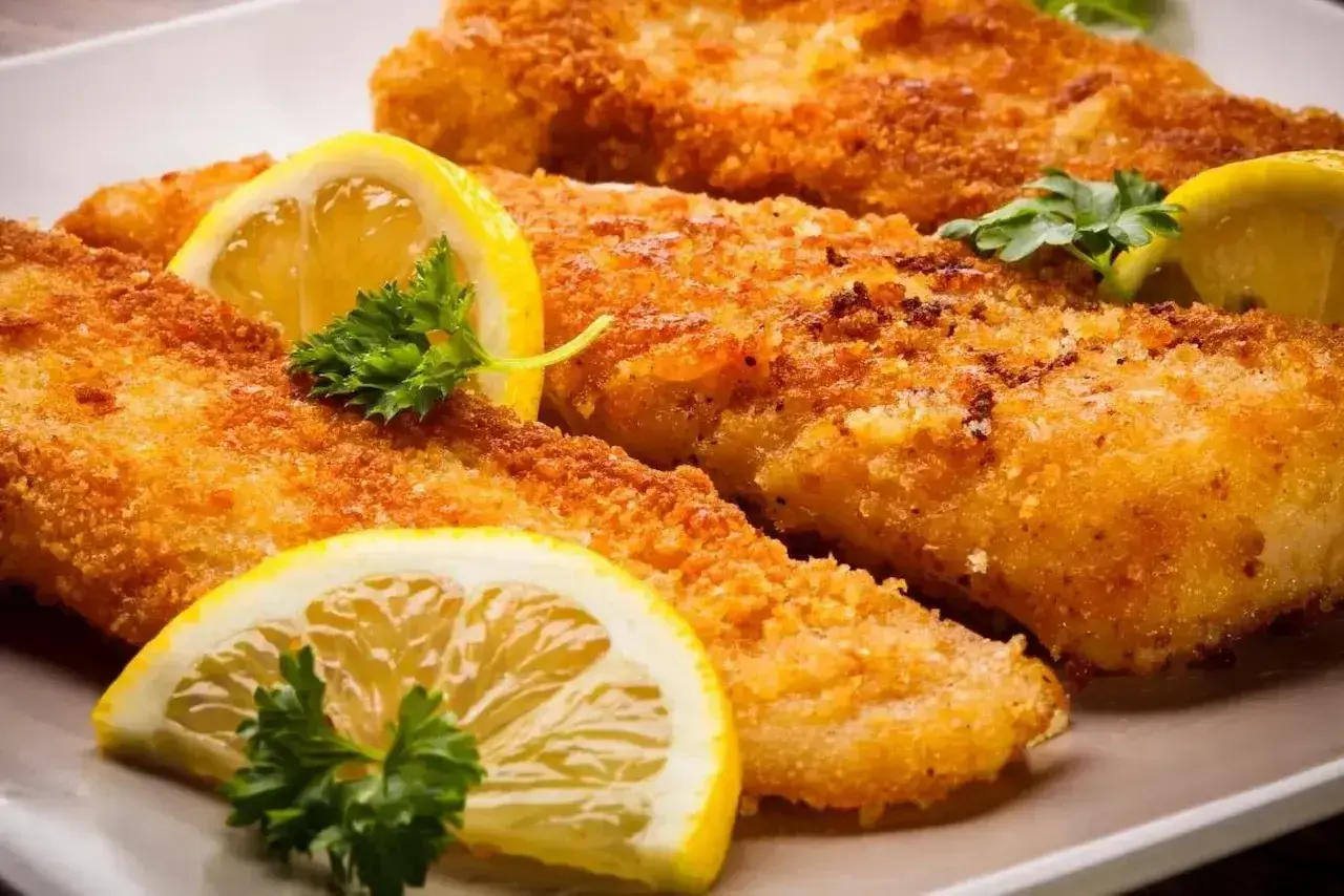 Chrupiące filety rybne w panierce panko, ozdobione plasterkami cytryny i natką pietruszki, kuszą apetycznym wyglądem.