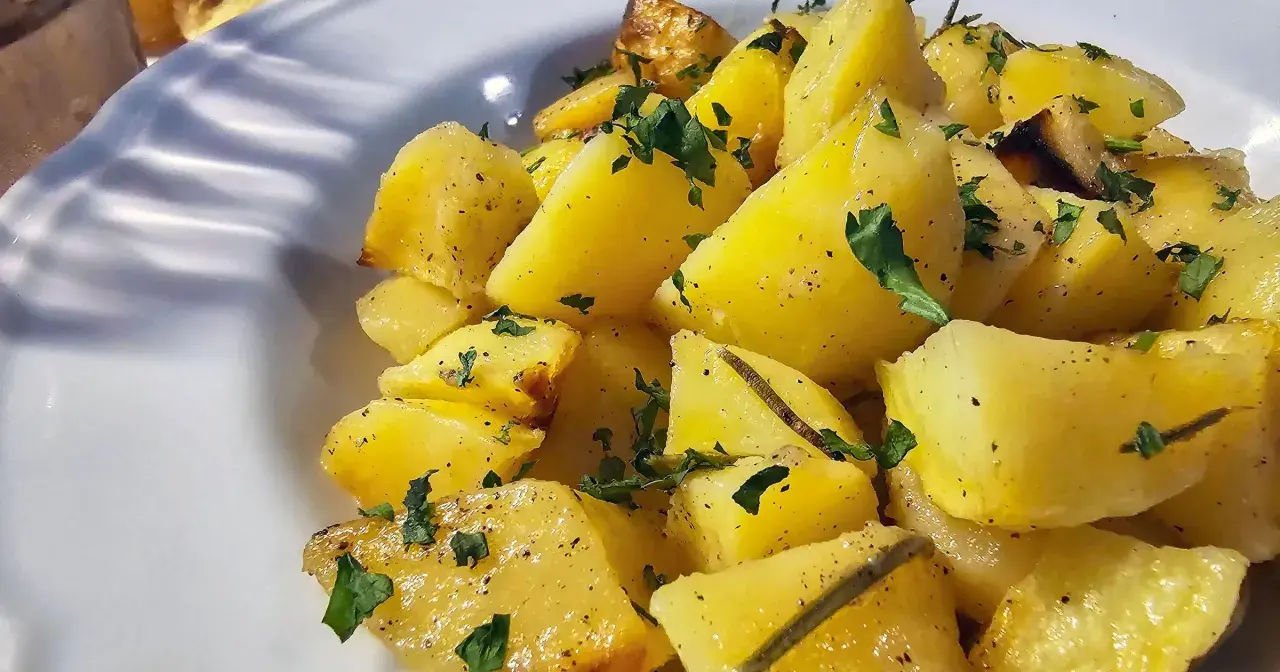 Pieczone ziemniaki pokrojone w ćwiartki, posypane natką pietruszki i pieprzem, podane na białym talerzu.