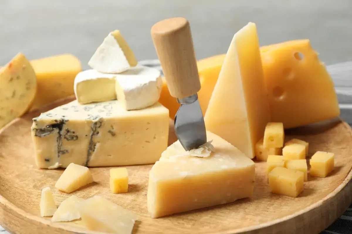 Różnorodne rodzaje serów: pleśniowy, camembert, parmezan i żółte sery, ułożone na drewnianej desce, gotowe do degustacji.