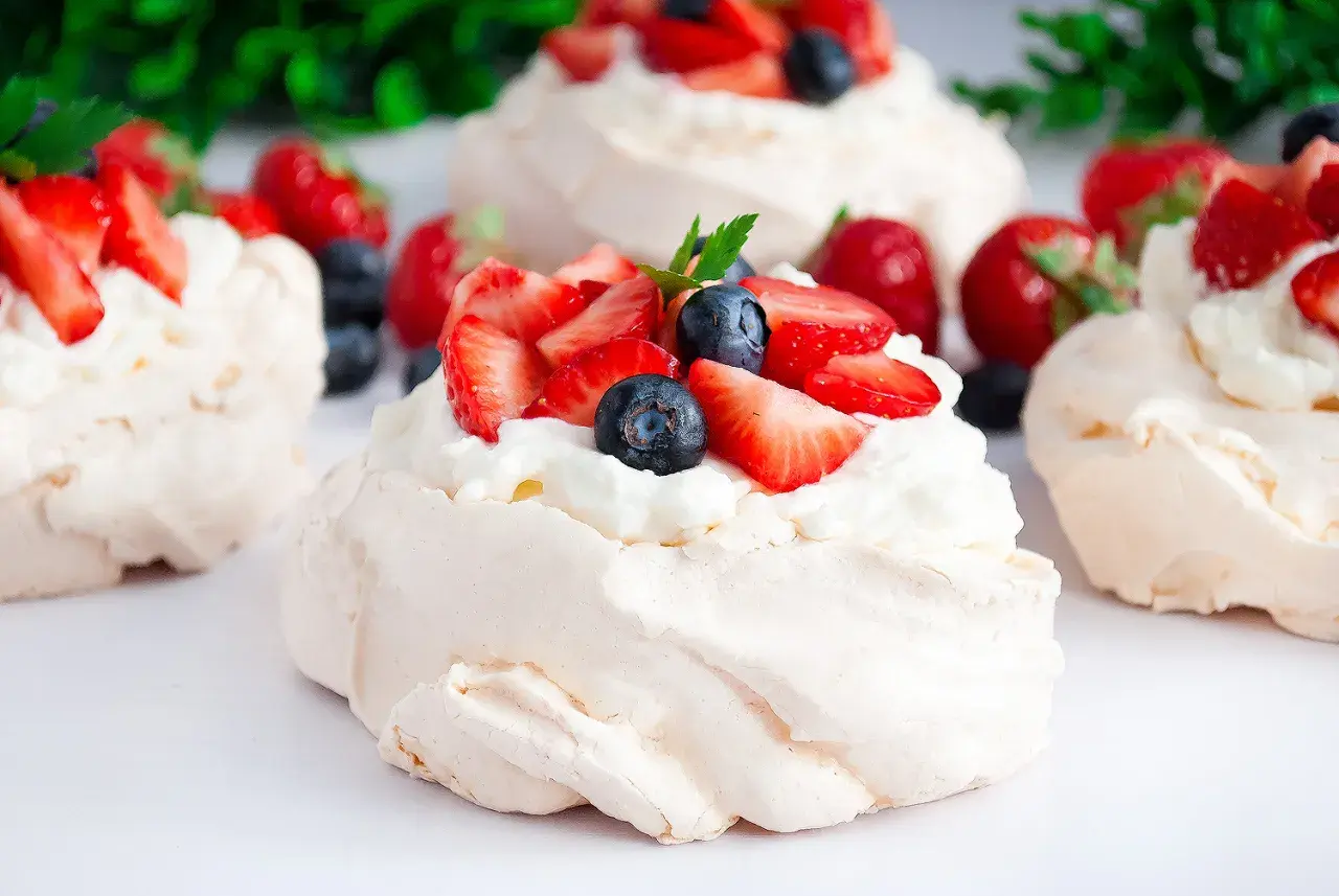 Mini bezy Pavlova z bitą śmietaną, truskawkami i borówkami. Delikatne, chrupiące na zewnątrz i miękkie w środku.