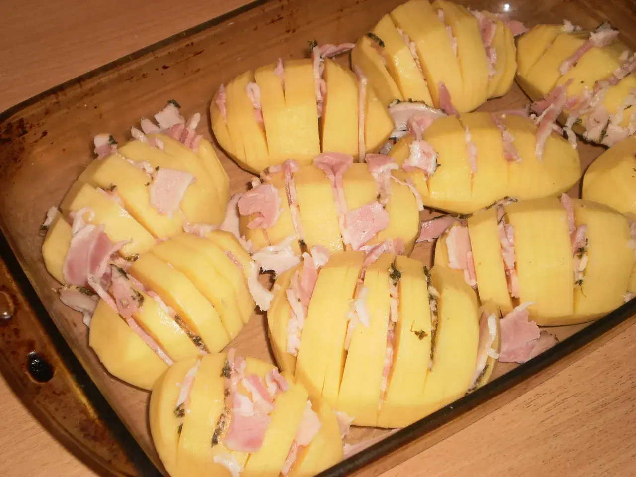 Ziemniaki hasselback z boczkiem i serem, gotowe do pieczenia w naczyniu żaroodpornym.