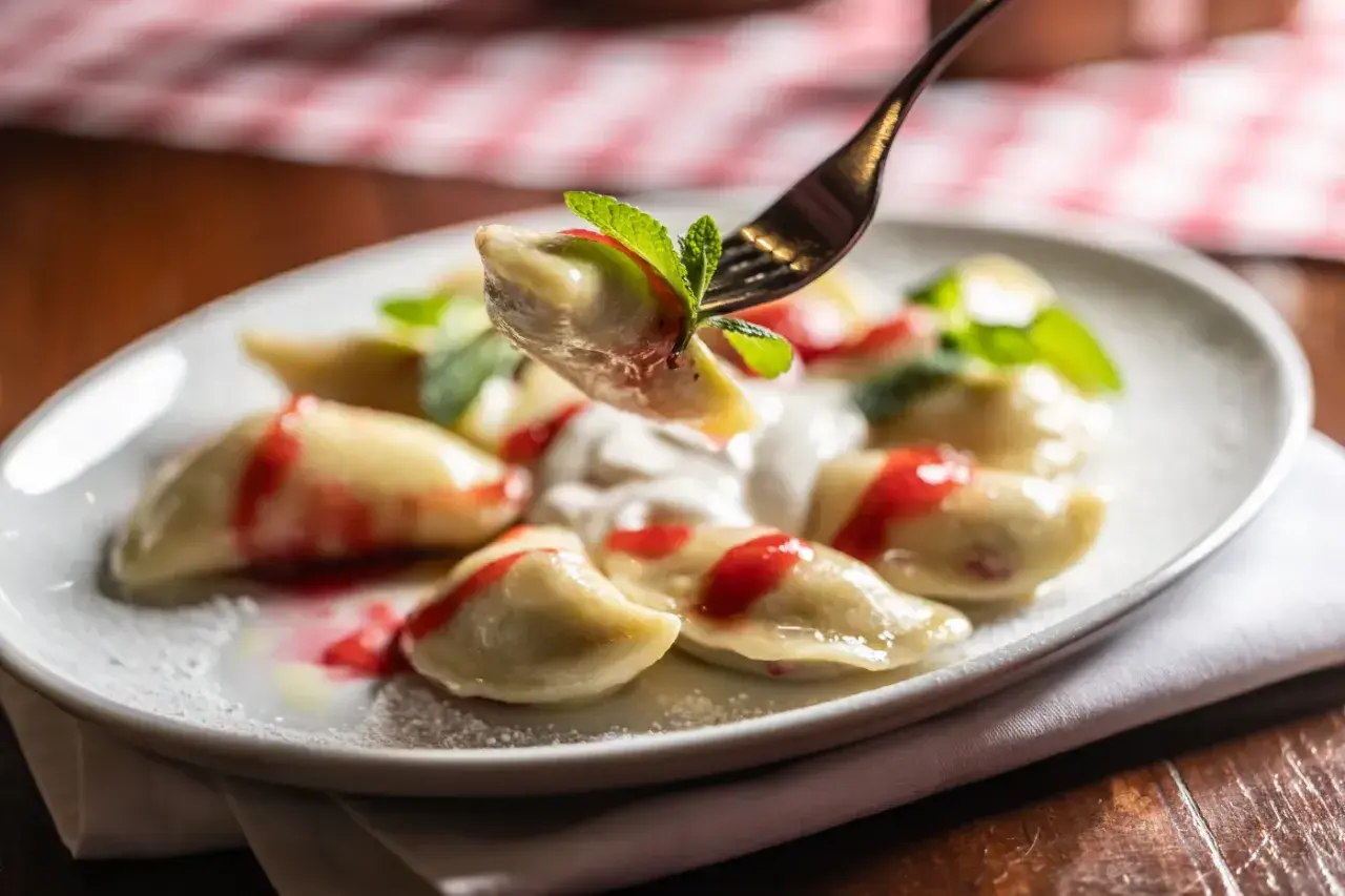 Jak gotować mrożone pierogi? Na talerzu pyszne pierogi z polewą truskawkową i miętą.