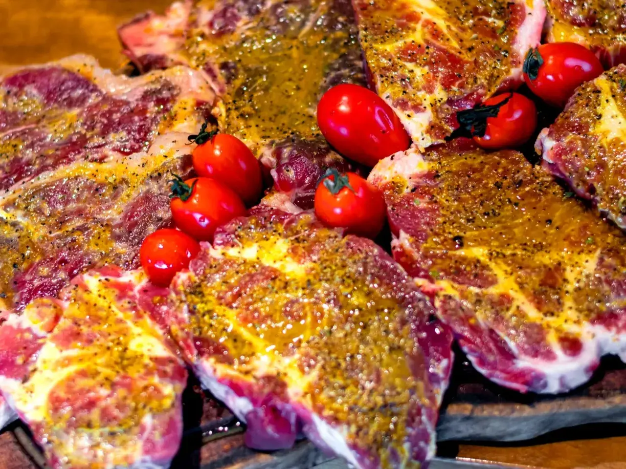 Karkówka wieprzowa, marynowana i przyprawiona, gotowa do grillowania, z pomidorkami koktajlowymi.