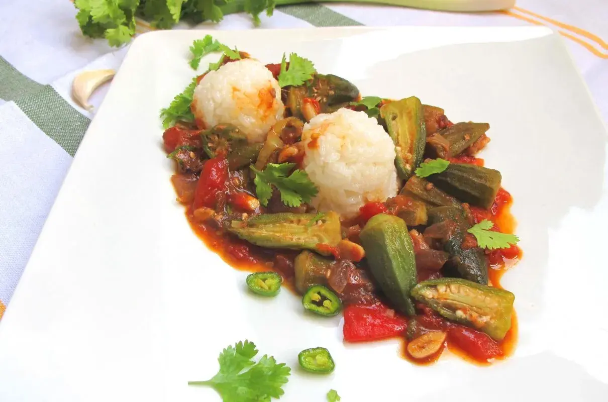 Pyszne okra przepisy na talerzu: duszona okra z pomidorami i ryżem, ozdobione kolendrą i papryczką chili.