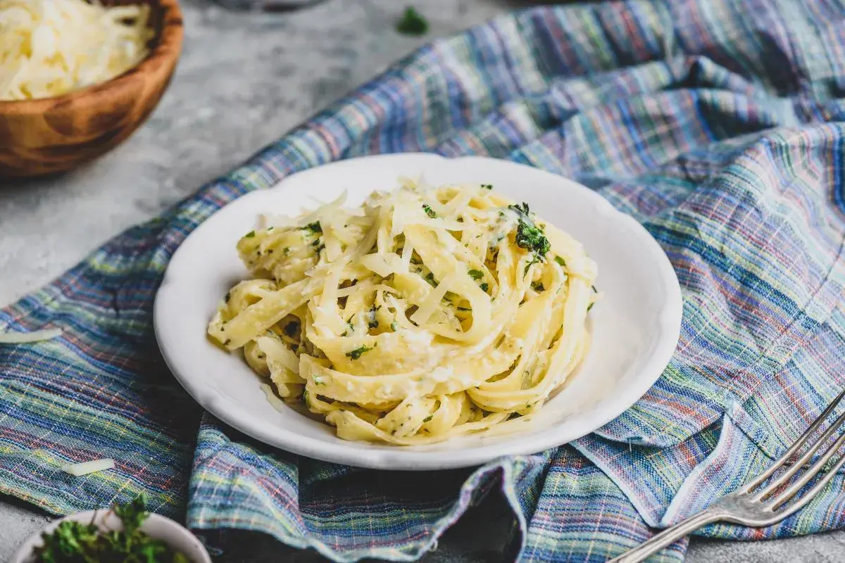 Pyszne fettuccine alfredo, bogato posypane parmezanem, na talerzu z kolorową serwetką.