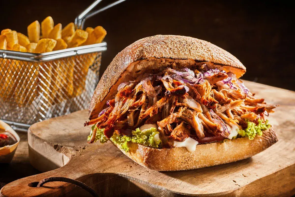 Apetyczny burger z szarpaną wieprzowiną, chrupiącymi frytkami i świeżą sałatą na drewnianej desce.
