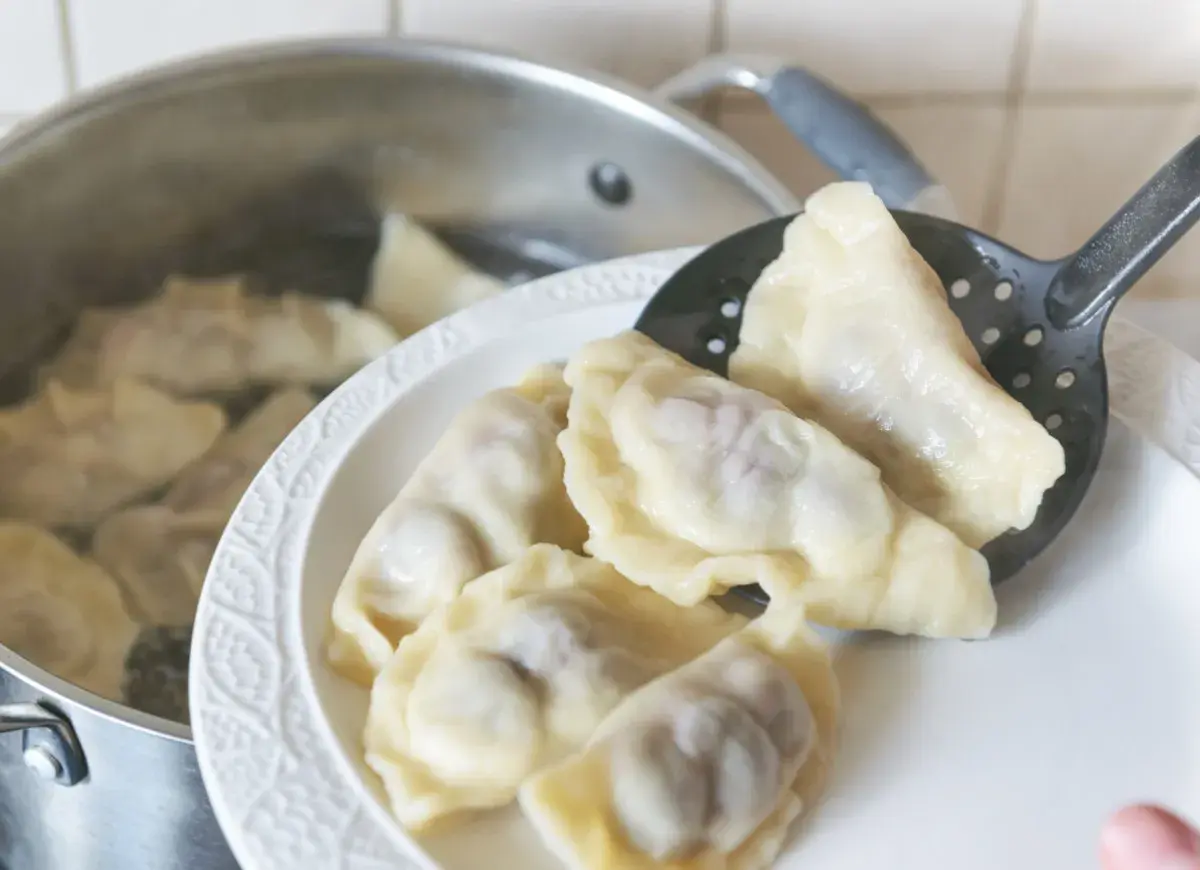 Gorące pierogi wyjmowane łyżką cedzakową z garnka. Czy pierogi przelewa się zimną wodą? Nie, gorące prosto z wody na talerz.