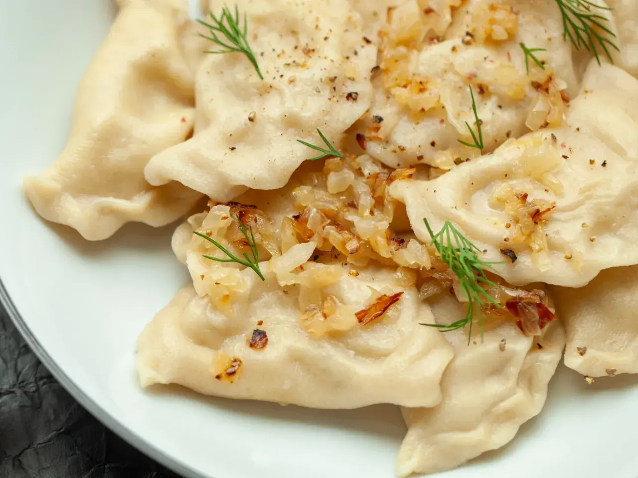 Pyszne pierogi z ziemniakami, okraszone cebulką i koperkiem, posypane pieprzem.