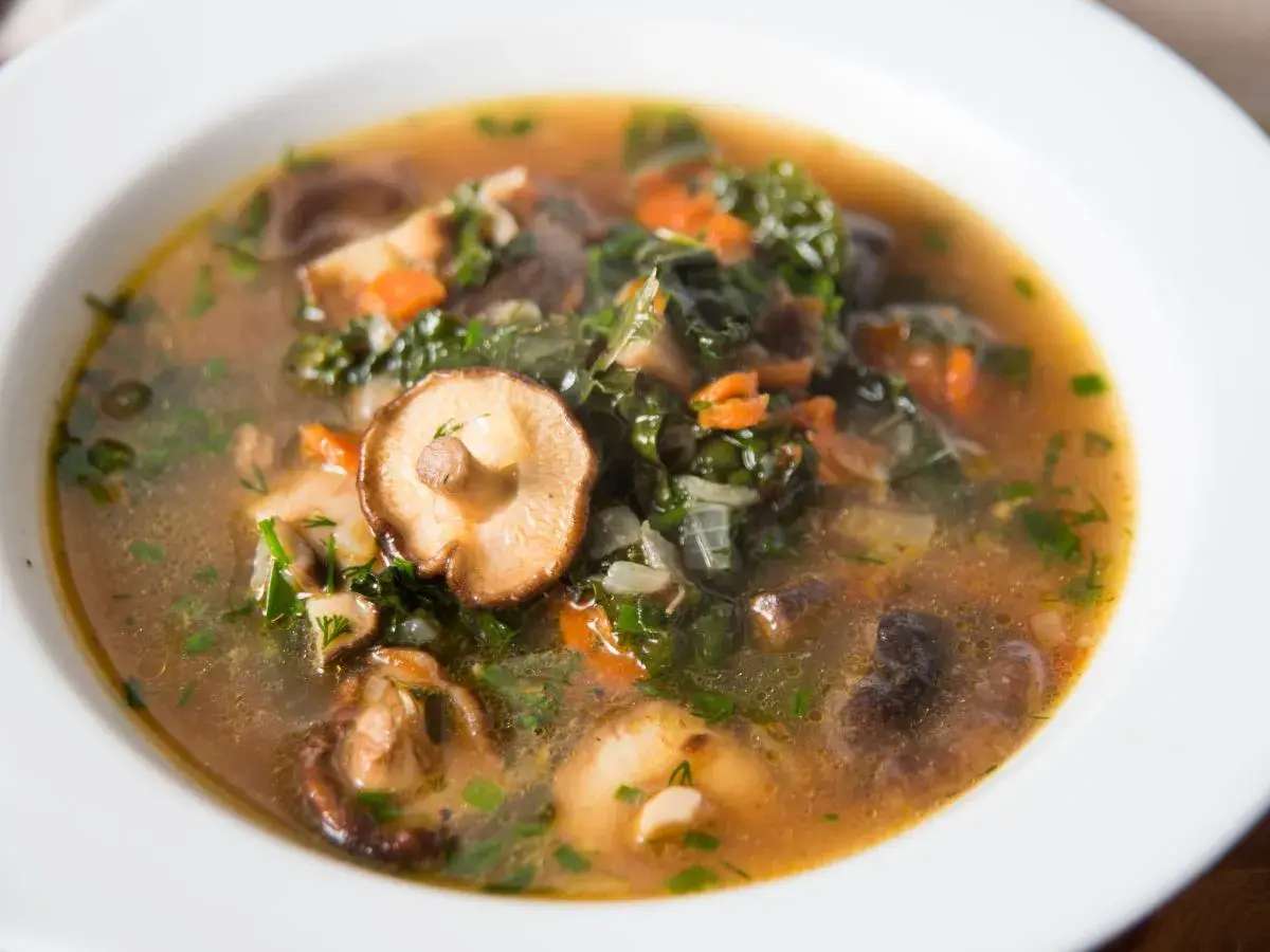 Aromaticzna, tradycyjna zupa grzybowa z kawałkami grzybów shiitake, zielonymi liśćmi i marchewką, podana w białej misce.