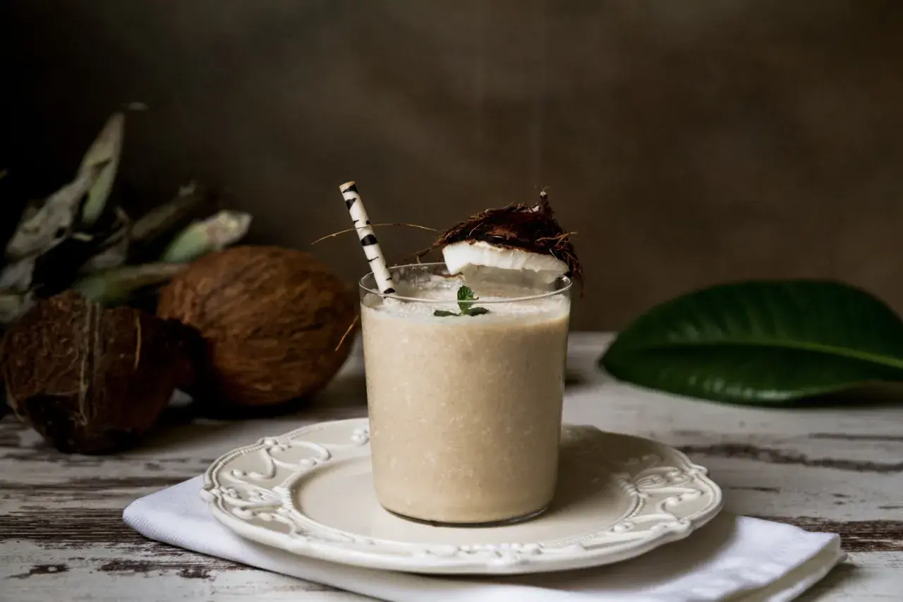 Jak zrobić mleko kokosowe? Pyszny napój z kokosa, ozdobiony miętą i kawałkiem owocu, gotowy do podania.