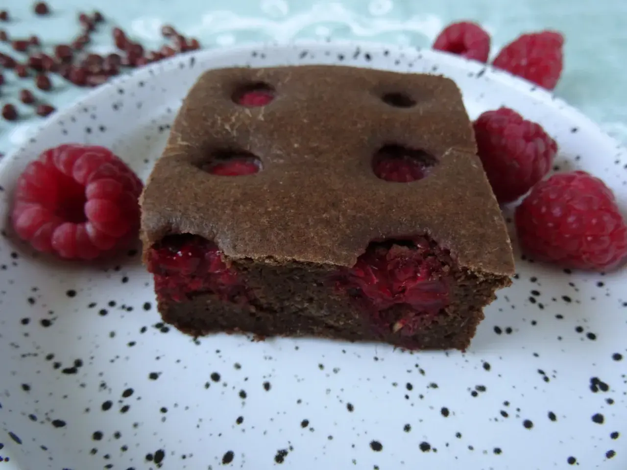 Pyszny fit brownie z fasoli, z malinami w środku i na talerzu. Idealny deser dla łasuchów.