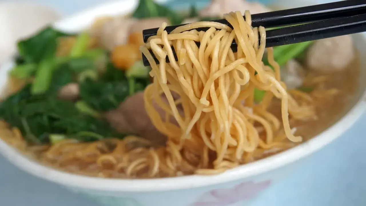 Chopsticks unoszą kłębek złocistego makaronu z miski pełnej aromatycznej domowej zupki chińskiej z warzywami i mięsem.