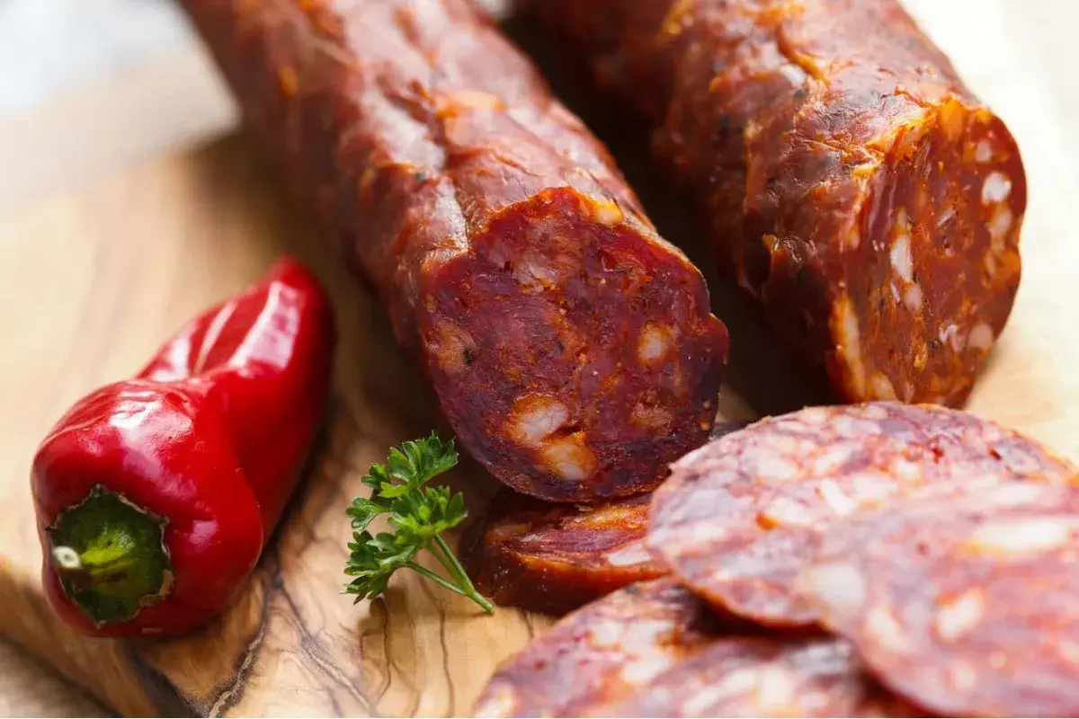 Kawałki pikantnego chorizo, czerwona papryczka i natka pietruszki na desce. To właśnie chorizo, co to za przysmak!