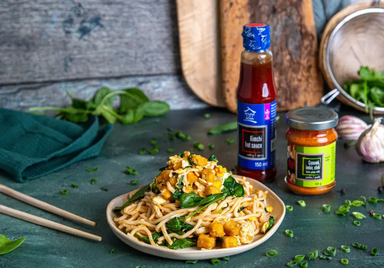 Pyszny makaron po koreańsku z tofu, szpinakiem i sosem kimchi. Obok butelka sosu i słoiczek pasty czosnek-imbir-chili.