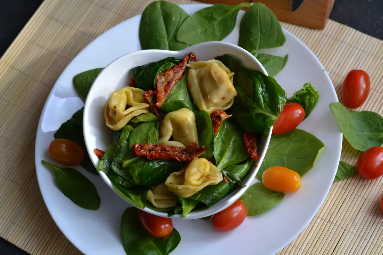 Pyszne tortellini z suszonymi pomidorami i świeżym szpinakiem, ozdobione pomidorkami koktajlowymi.