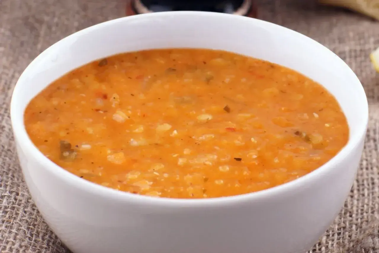Gęsta, pomarańczowa zupa dhal w białej misce, podana na lnianym obrusie.
