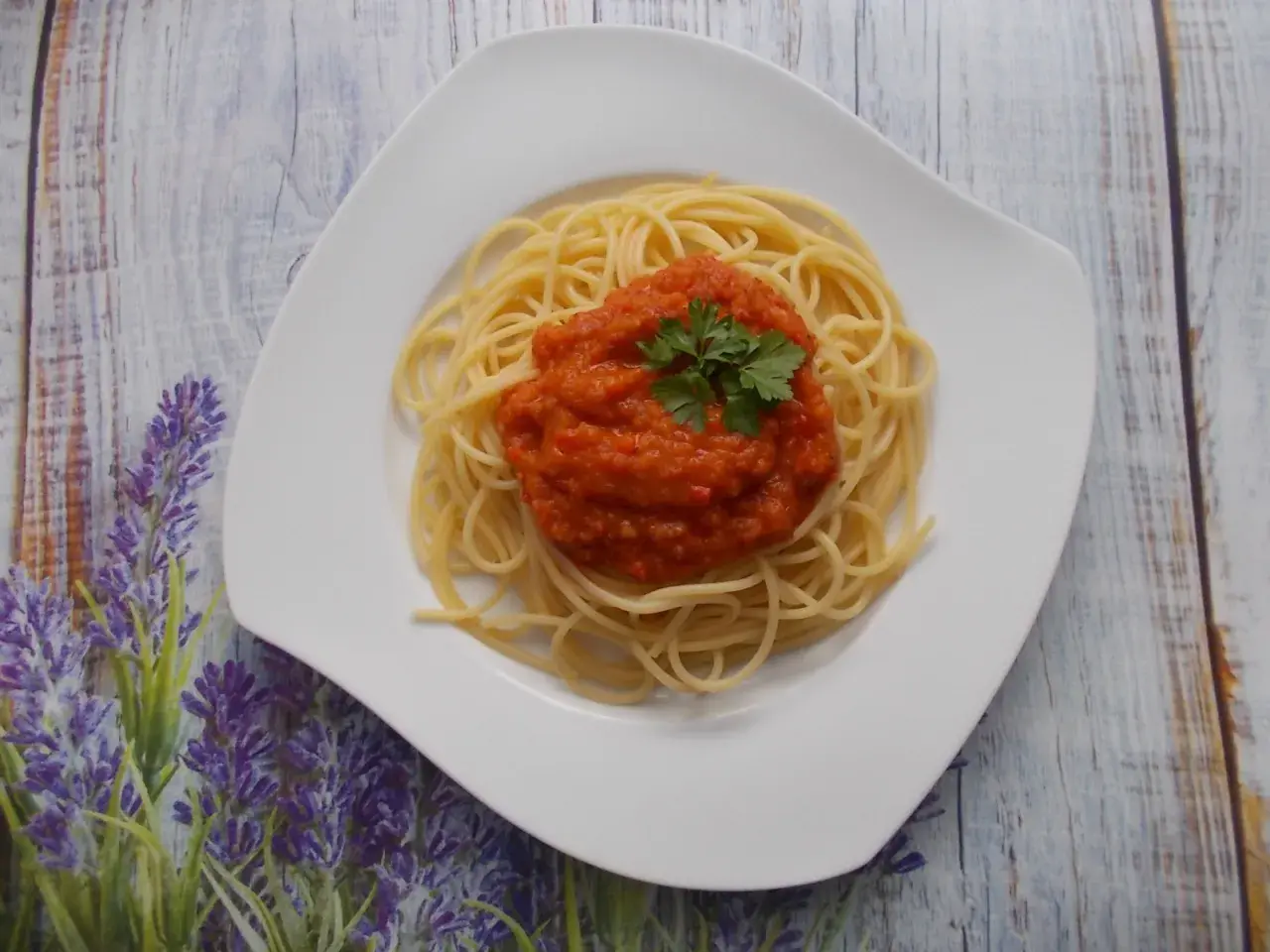 Spaghetti ze świeżych pomidorów, udekorowane natką pietruszki, na białym talerzu, na tle drewnianego blatu i lawendy.
