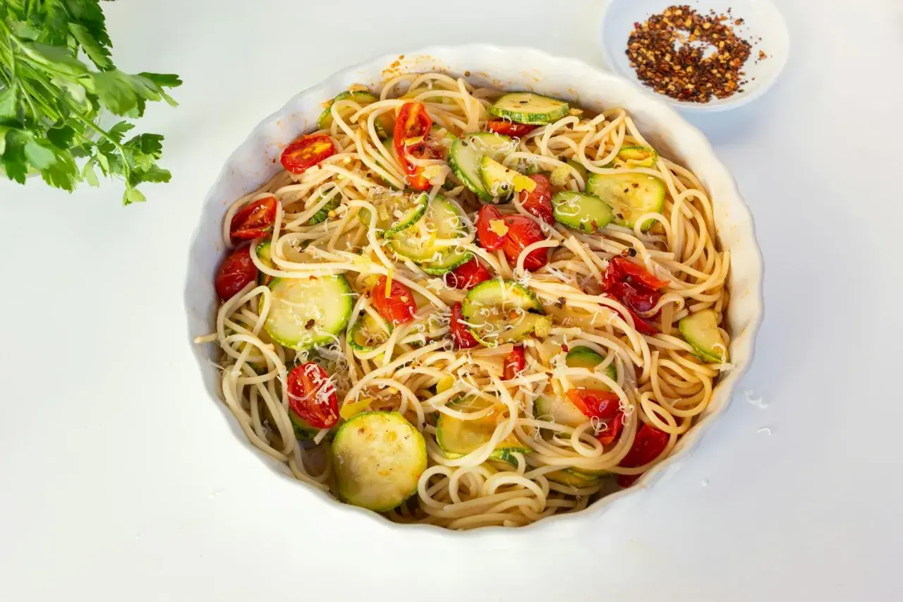 Pyszny makaron z cukinią, pomidorkami i parmezanem, posypany płatkami chili.