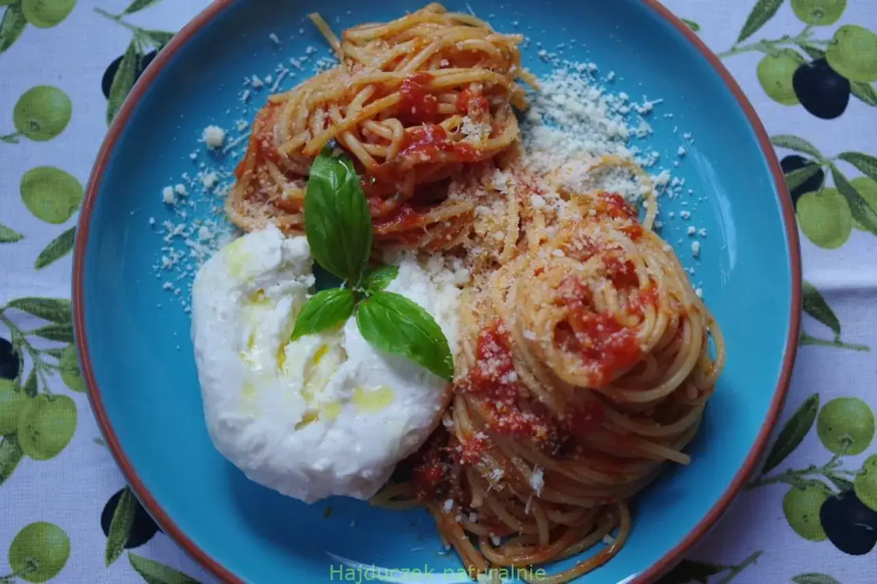 Pyszne spaghetti z pomidorami, polane oliwą, z kulką burraty i listkiem bazylii.
