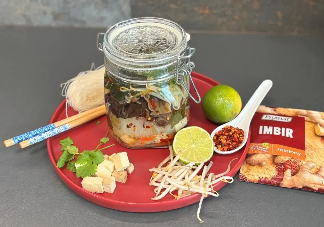 Słoik z warzywami, makaronem i tofu, gotowy na domową zupkę chińską. Obok limonka, chili i imbir.