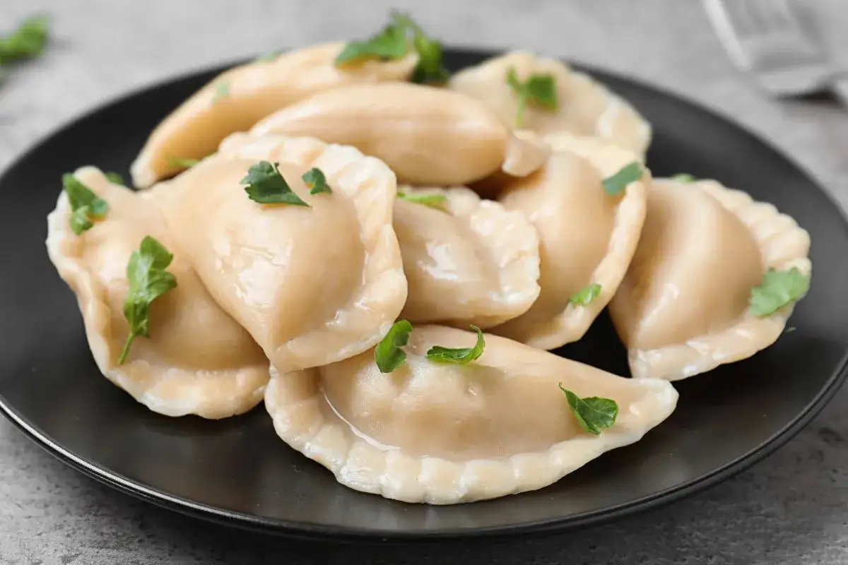 Pyszne, parujące pierogi na czarnym talerzu, ozdobione natką pietruszki. Czy pierogi przelewa się zimną wodą? Nie, te wyglądają na idealnie ugotowane!
