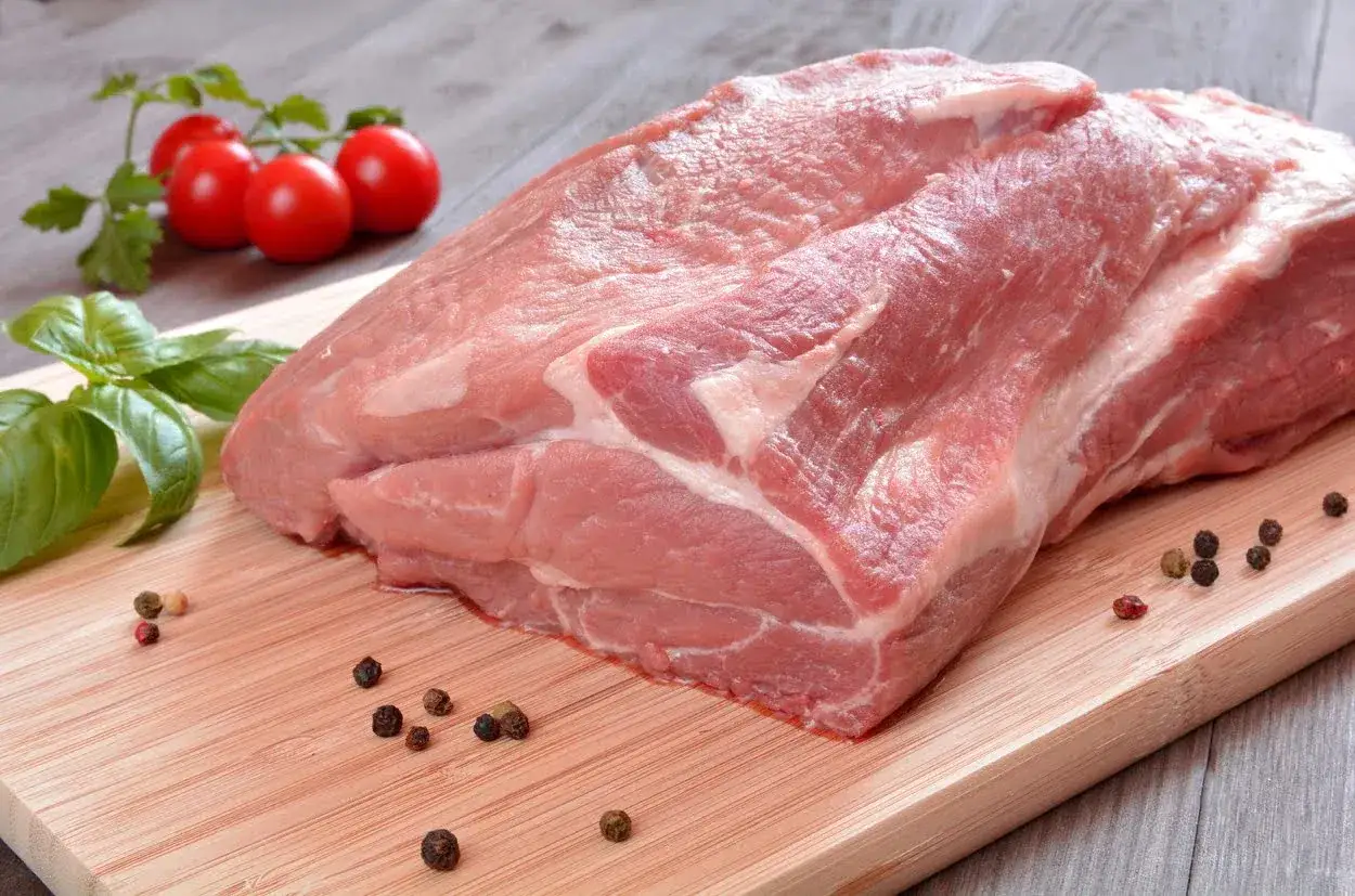 Surowa karkówka wieprzowa, gotowa do pieczenia. Obok świeża bazylia, pomidorki i ziarna pieprzu.