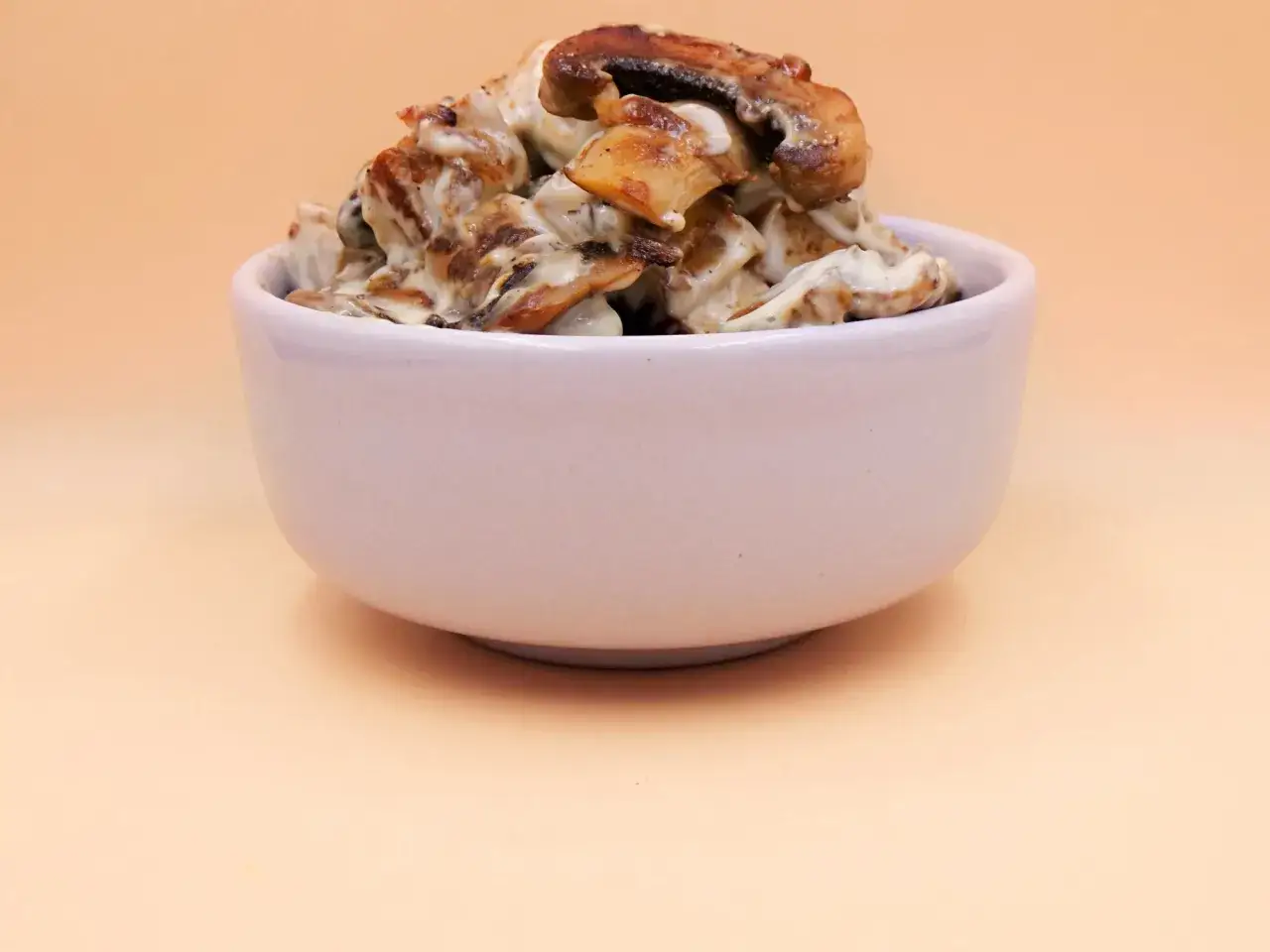 Tofu z pieczarkami w kremowym sosie, podane w białej miseczce.
