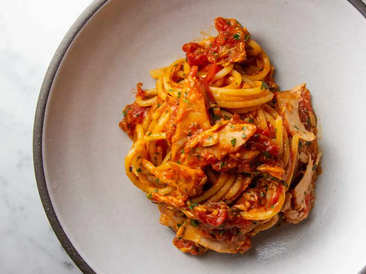 Pyszne spaghetti z tuńczykiem po włosku, podane w sosie pomidorowym z ziołami. Idealne na szybki obiad.