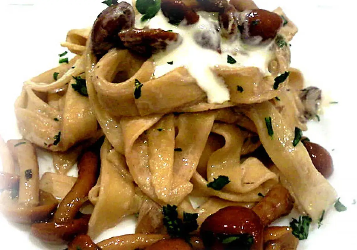 Pyszne dania z makaronem tagliatelle z grzybami i kremowym sosem, posypane natką pietruszki.