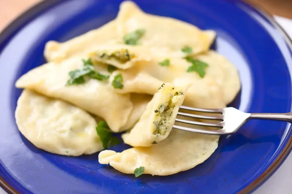 Pyszne pierogi ze szpinakiem i serem, udekorowane natką pietruszki, czekają na widelcu.