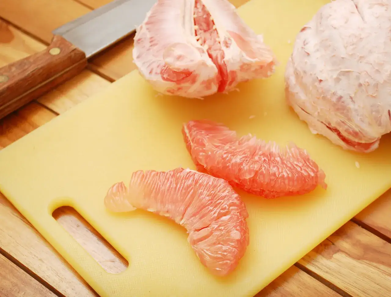 Jak jeść pomelo? Na desce leży obrany owoc i jego cząstki, obok nóż.