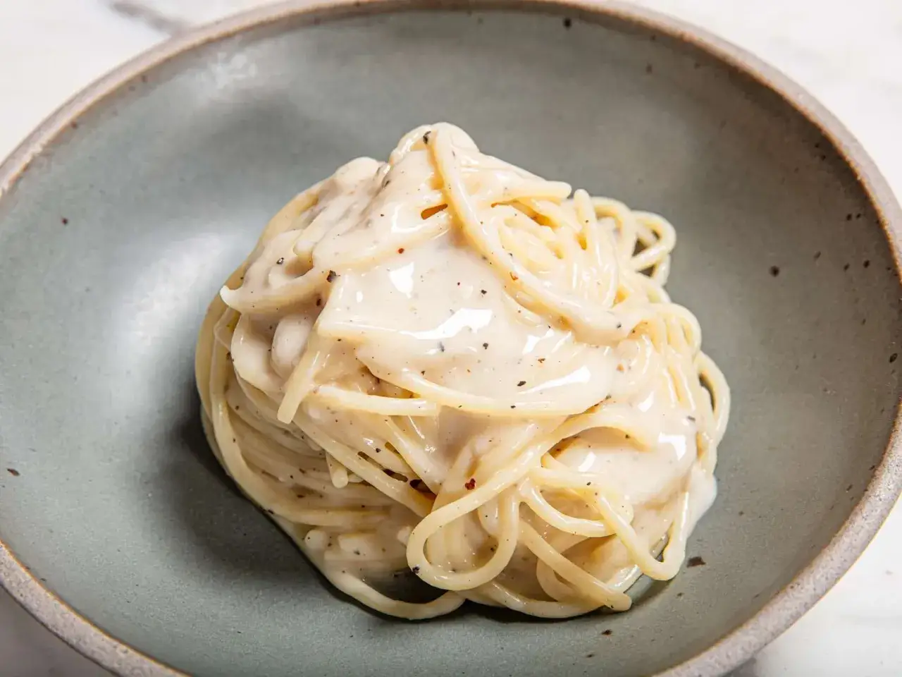 Porcja kremowego spaghetti z pieprzem, podana w szarej misce.