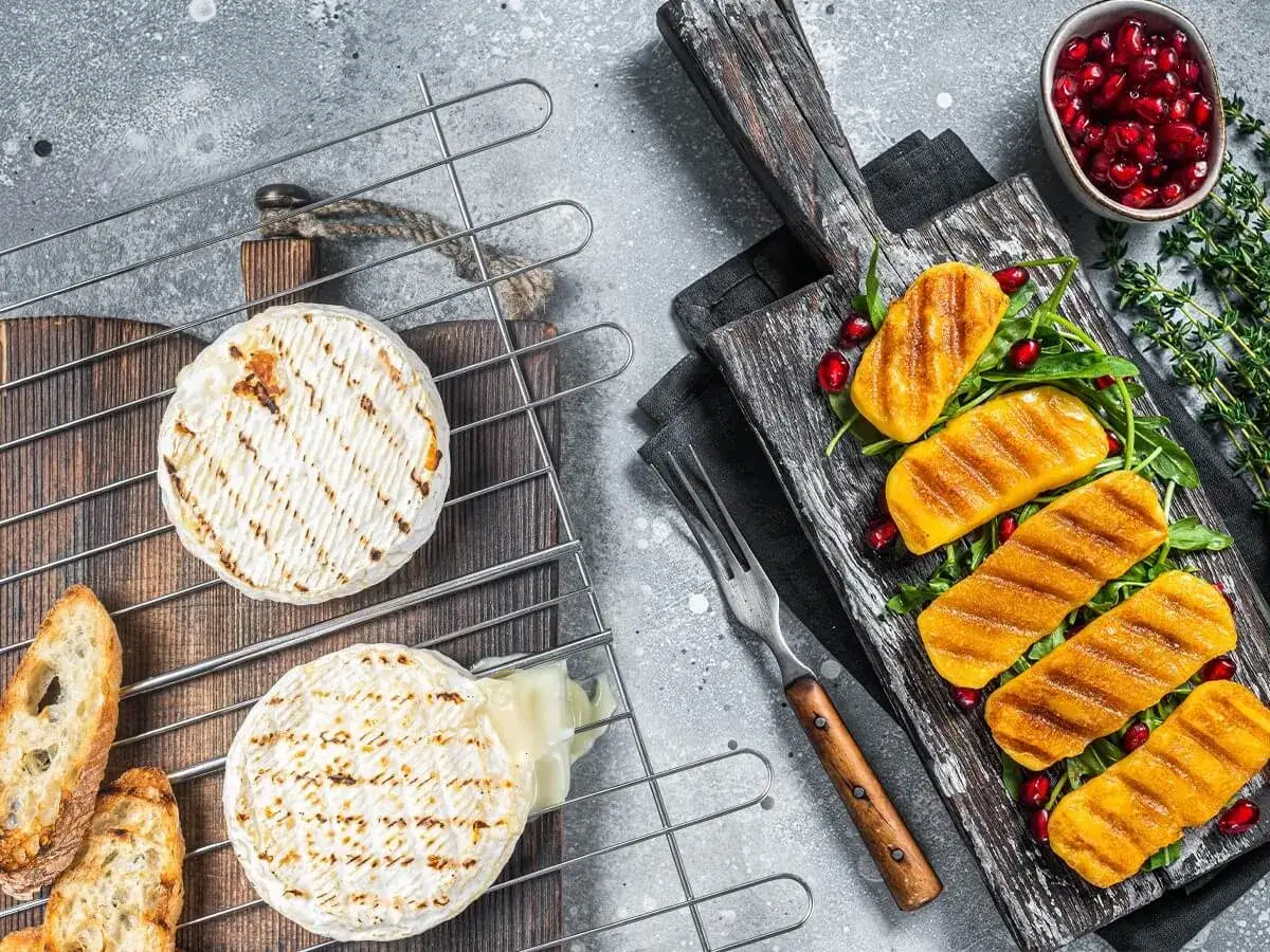 Dwa krążki sera camembert z grilla, jeden lekko roztopiony, obok pieczywo i grillowane dynie. Idealny jaki ser na grilla.
