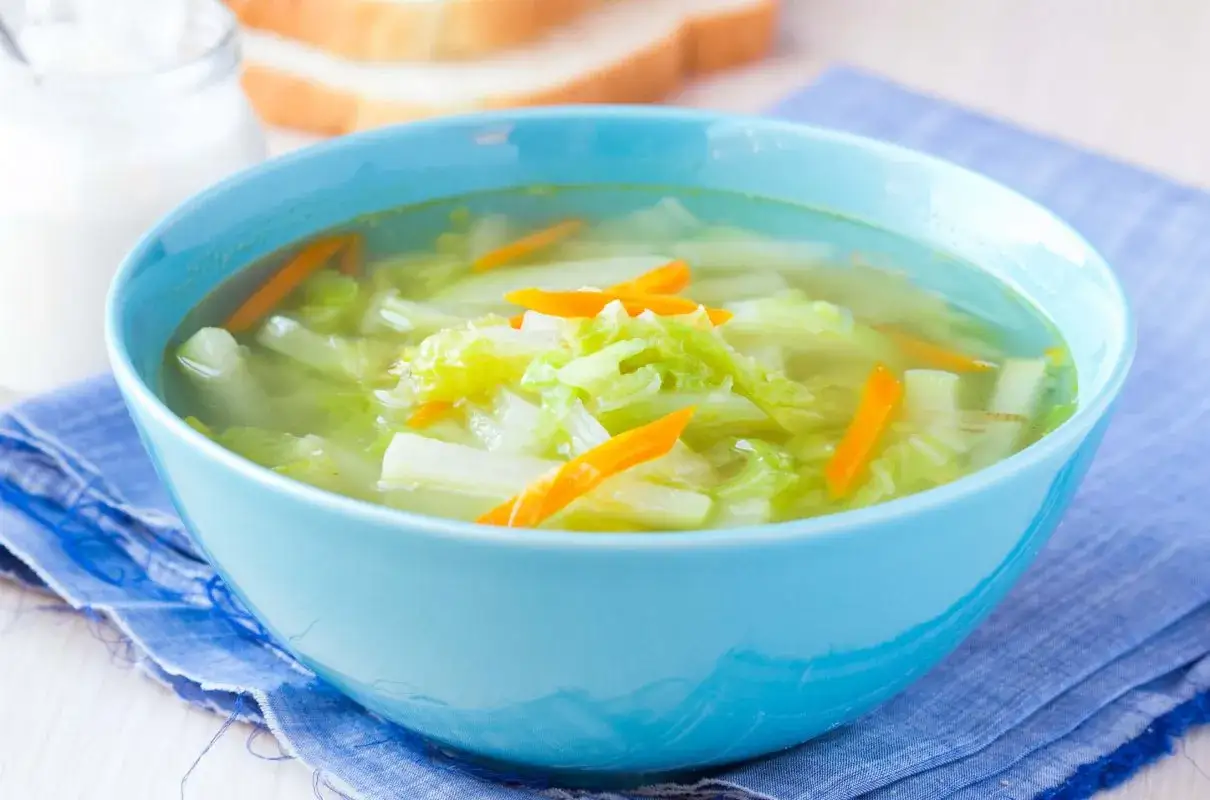 Aksamitna zupa z kalarepy i marchewki w błękitnej misce, podana z chlebem.