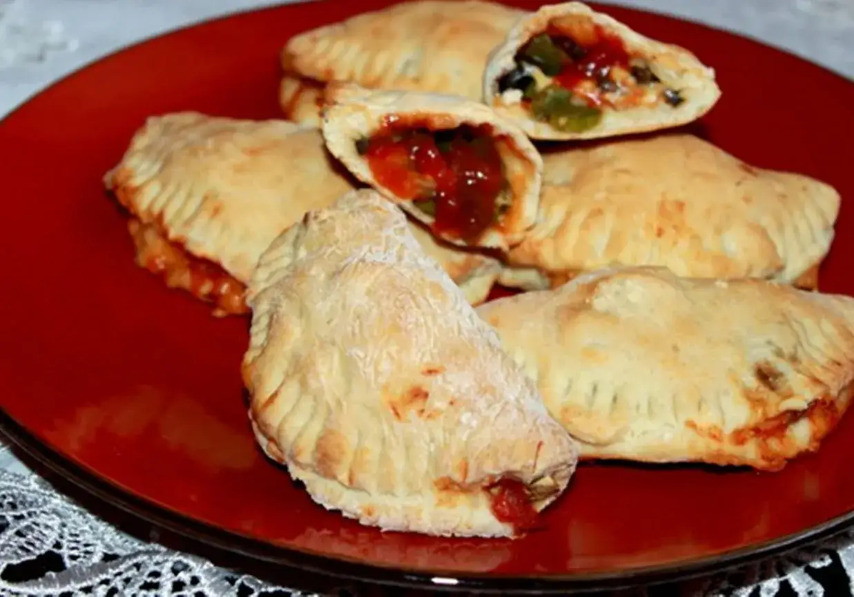 Pyszne pierogi pizza z farszem pomidorowym i warzywami, podane na czerwonym talerzu.