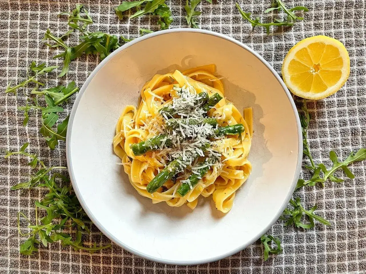 Pyszne tagliatelle ze szparagami, posypane parmezanem, z dodatkiem rukoli i cytryny.
